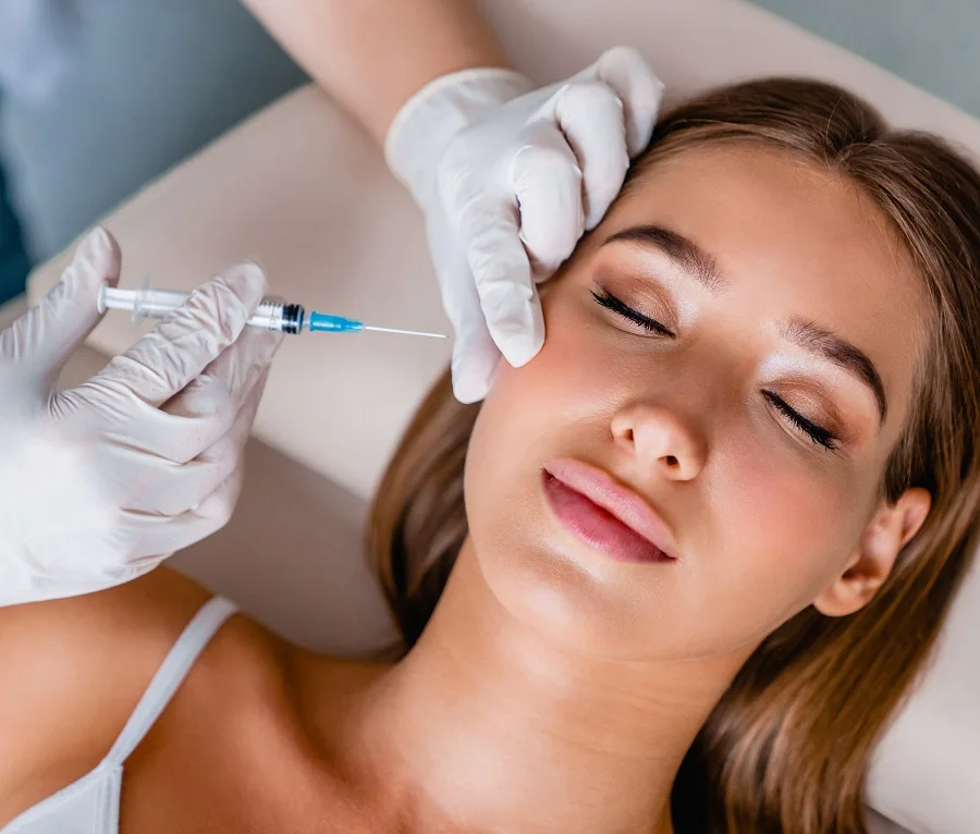 Médico preparando una inyección cosmética cerca de la mandíbula de una mujer.